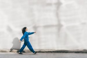 Mulher jovem de roupa azul caminhando em frente à parede branca — Foto: 1 de 1 M