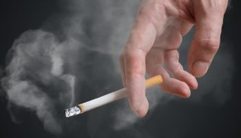 Foto colorida de homem segurando cigarro em fundo preto - Fumante passivo — Foto