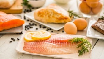 Peixe-tilapia-cru-no-prato-frango-e-ovos-no-fundo