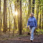 Mulher caminhando em um parque iluminado pelo sol ao pôr do sol na primavera — F