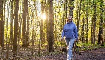 Mulher caminhando em um parque iluminado pelo sol ao pôr do sol na primavera — F