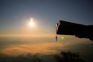 Silhouette of human hand holding bible and cross, the background